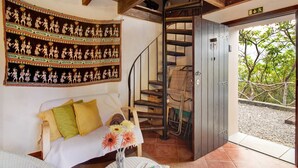 A room with a bed, a wall tapestry, a spiral staircase, and a door leading outside. - Vacation Chalet "The Perfect Cottage" with Mountain View & Wi-Fi (São Vicente)