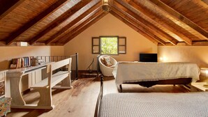 A cozy attic bedroom with a sloped wooden ceiling, a bed, a chair, a small table, and a window with a view of greenery. - Vacation Chalet "The Perfect Cottage" with Mountain View & Wi-Fi (São Vicente)
