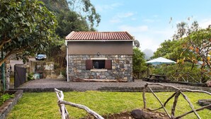A stone building with a tiled roof, a window with shutters, and a paved area in front. - Vacation Chalet "The Perfect Cottage" with Mountain View & Wi-Fi (São Vicente)