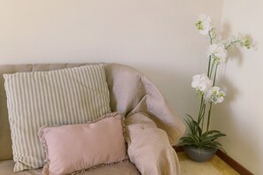 Un coin de pièce avec un canapé beige, des coussins à rayures et roses, et une plante orchidée en pot.