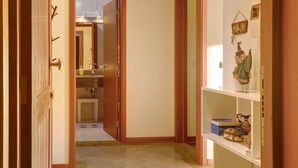 A hallway with a door leading to a bathroom, a shelf with decorative items, and a tiled floor. - Holiday Apartment Oliveira Atlantic View with Sea View, Wi-Fi & Balcony (Funchal)