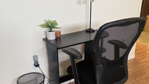 A black office chair with a mesh backrest, a black desk with a white plant and a candle, and a black trash can.