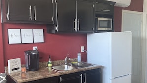 A kitchen with dark cabinets, a white refrigerator, a microwave, and a granite countertop. There are three framed signs on the wall and a small plant on top of the microwave.