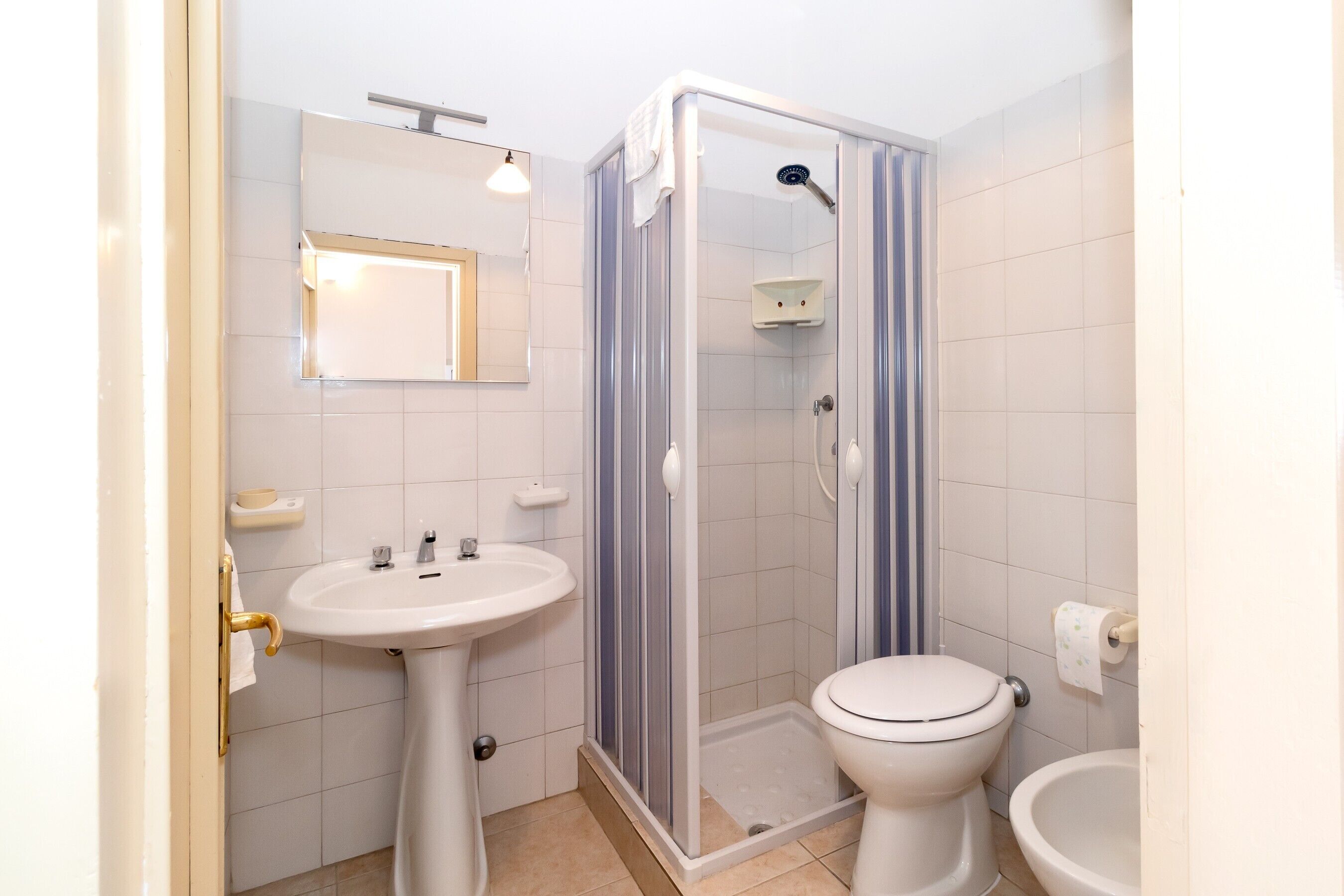 A bathroom with a pedestal sink, a toilet, a shower enclosure, and a mirror.
