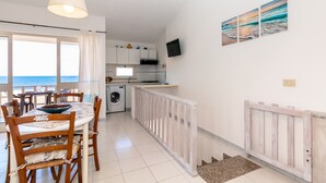 A kitchen with a view of the sea, a dining area with chairs, a washing machine, and a TV on the wall. - Apartment "Vista Corsica" on Isola Rossa with Sea View & Terrace (Isola Rossa)