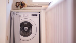 A front-loading washing machine in a laundry room with a window above it. - Apartment "Vista Corsica" on Isola Rossa with Sea View & Terrace (Isola Rossa)