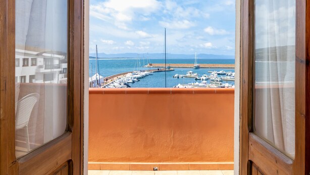 Uitzicht vanaf een balkon op een jachthaven met boten, een heldere lucht en op de achtergrond bergen.