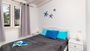 A bedroom with a bed, a nightstand, a window with curtains, and wall art. - Apartment "Vista Bocche di Bonifacio" with Outdoor Pool (Isola Rossa)