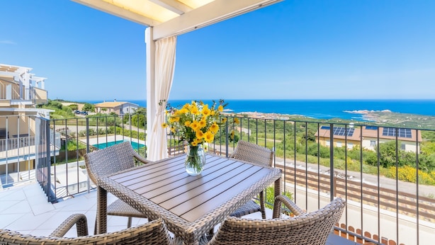 A balcony with wicker furniture, a vase of flowers, and a view of the sea. - Apartment "Vista Bocche di Bonifacio" with Outdoor Pool (Isola Rossa)