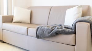 A beige sofa with a grey blanket and two white pillows. - Apartment "Vista Bocche di Bonifacio" with Outdoor Pool (Isola Rossa)