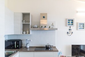 Cozinha moderna com micro-ondas, chaleira e liquidificador na bancada, forno embutido e televisão.