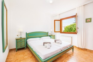 A room with a bed, two nightstands, a window with a view, and a radiator. - Holiday Home "Tomymar" with Pool, Wi-Fi, Garden, and Terrace (Cala Ratjada)