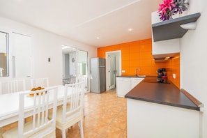 Eine moderne Küche mit weißen Schränken, einer orangefarbenen Spritzschutzwand und einem Essbereich mit weißen Stühlen und einem Tisch.