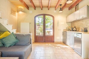 Una cocina con puerta de madera, un comedor con mesa y sillas, y un sofá gris con cojines.
