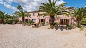 Un bâtiment doté d’une cour recouverte de gravier, de palmiers et d’un grand pot en argile.