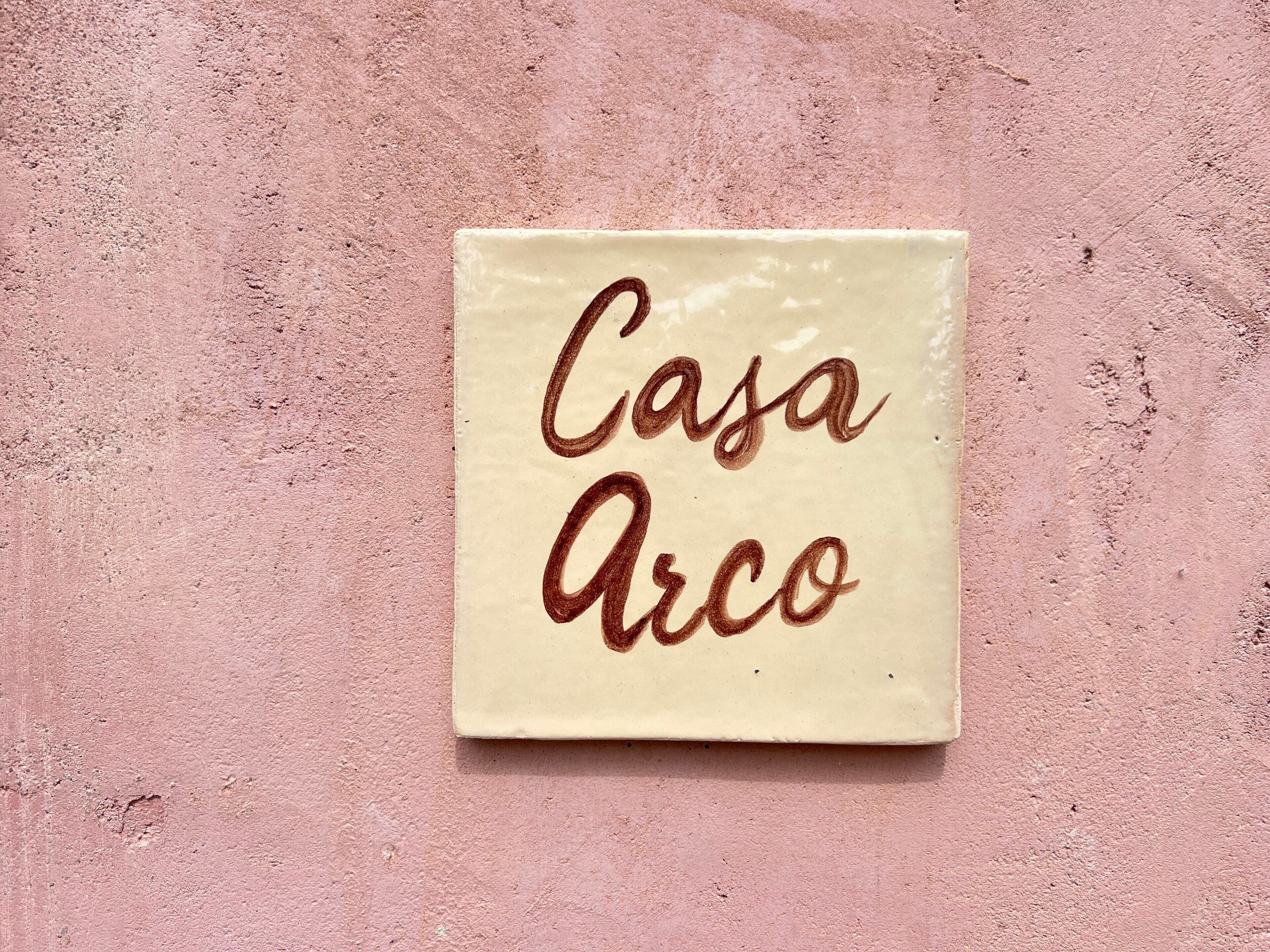 Un carreau de céramique de forme carrée, sur lequel on peut lire les mots « Casa Arco » écrits dans une police de caractères cursive.