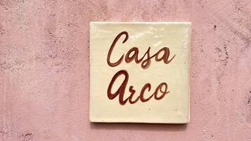 Un carreau de céramique de forme carrée, sur lequel on peut lire les mots « Casa Arco » écrits dans une police de caractères cursive.