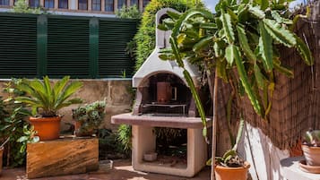 Een terras buiten met een barbecue van steen, planten in potten en een stenen bank.
