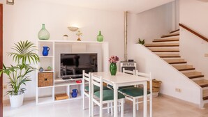 Una sala de estar con televisor, muebles blancos, una escalera y una planta en maceta.
