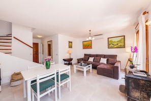 A living room with a sofa, a dining table with chairs, a lamp, and a painting on the wall.
