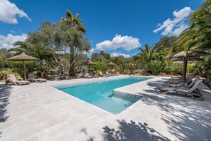 Une piscine entourée d’une végétation tropicale, agrémentée de chaises longues et de parasols en feuilles de palmier.