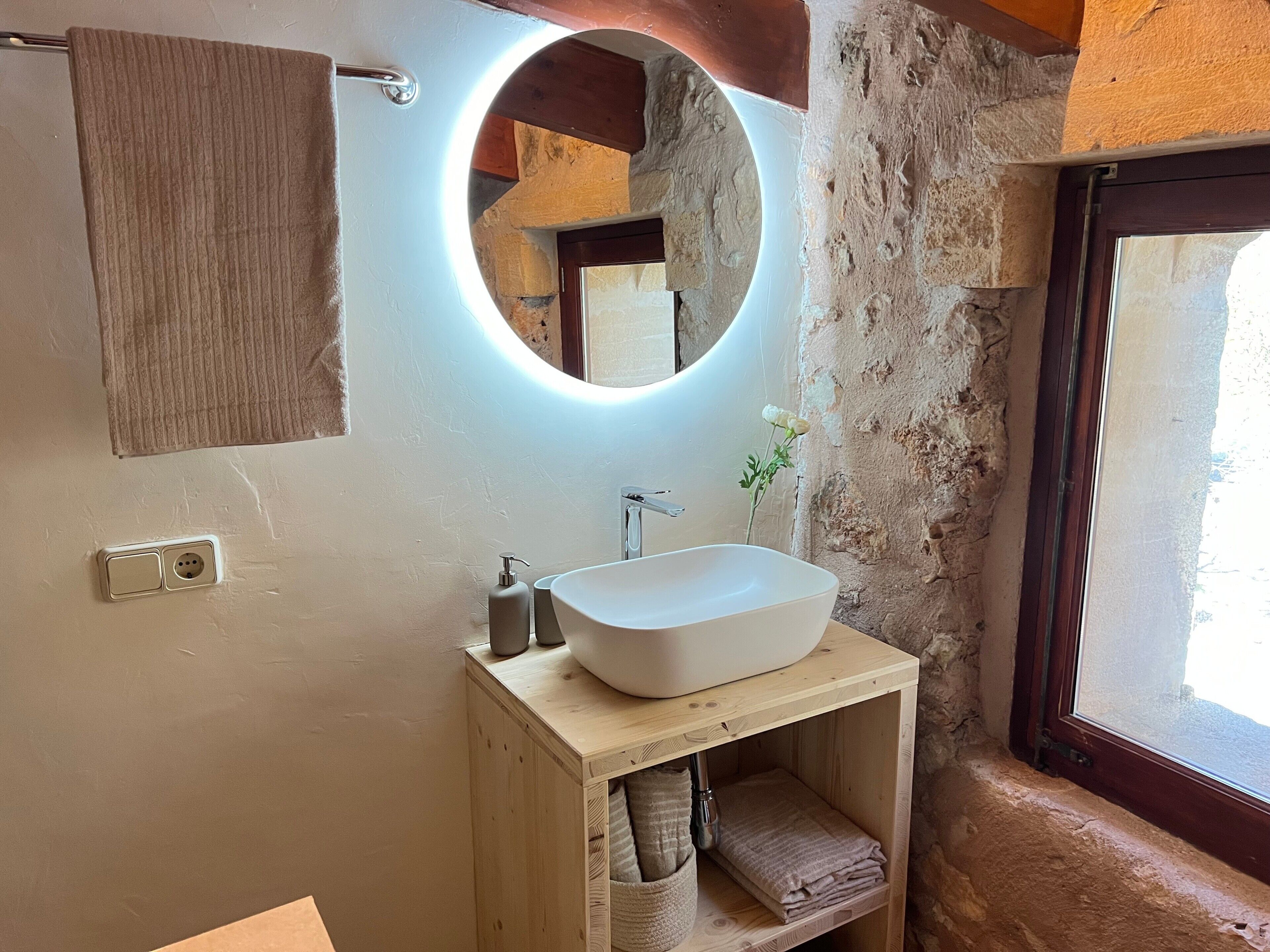 A bathroom with a wooden vanity, a white sink, a round mirror, and a towel rack.