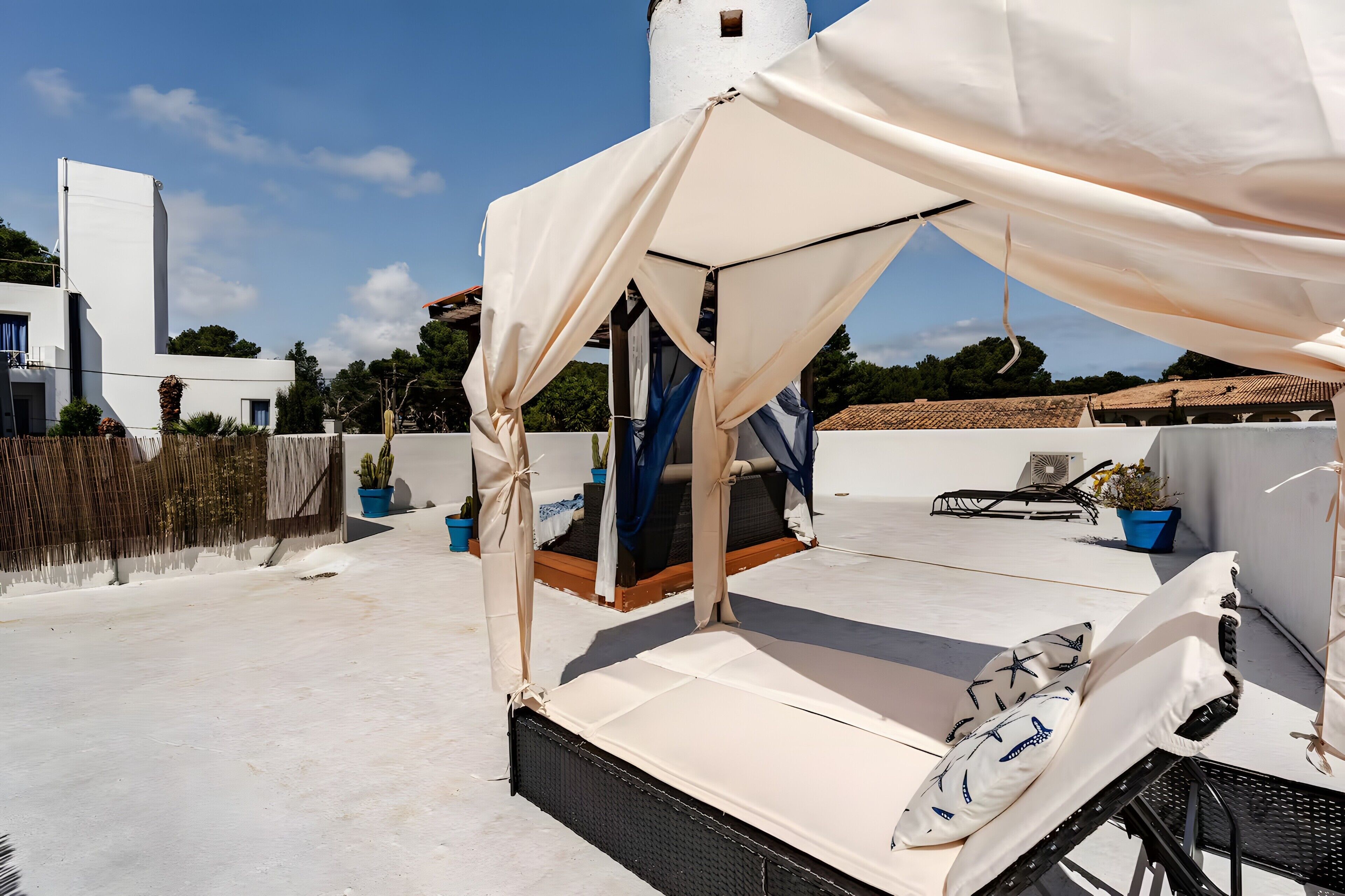 A rooftop terrace with a bed, a canopy, and potted plants.