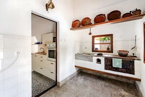 Een keuken met witte kasten, een patroon vloer, een houten plank met servies en een vintage fornuis.