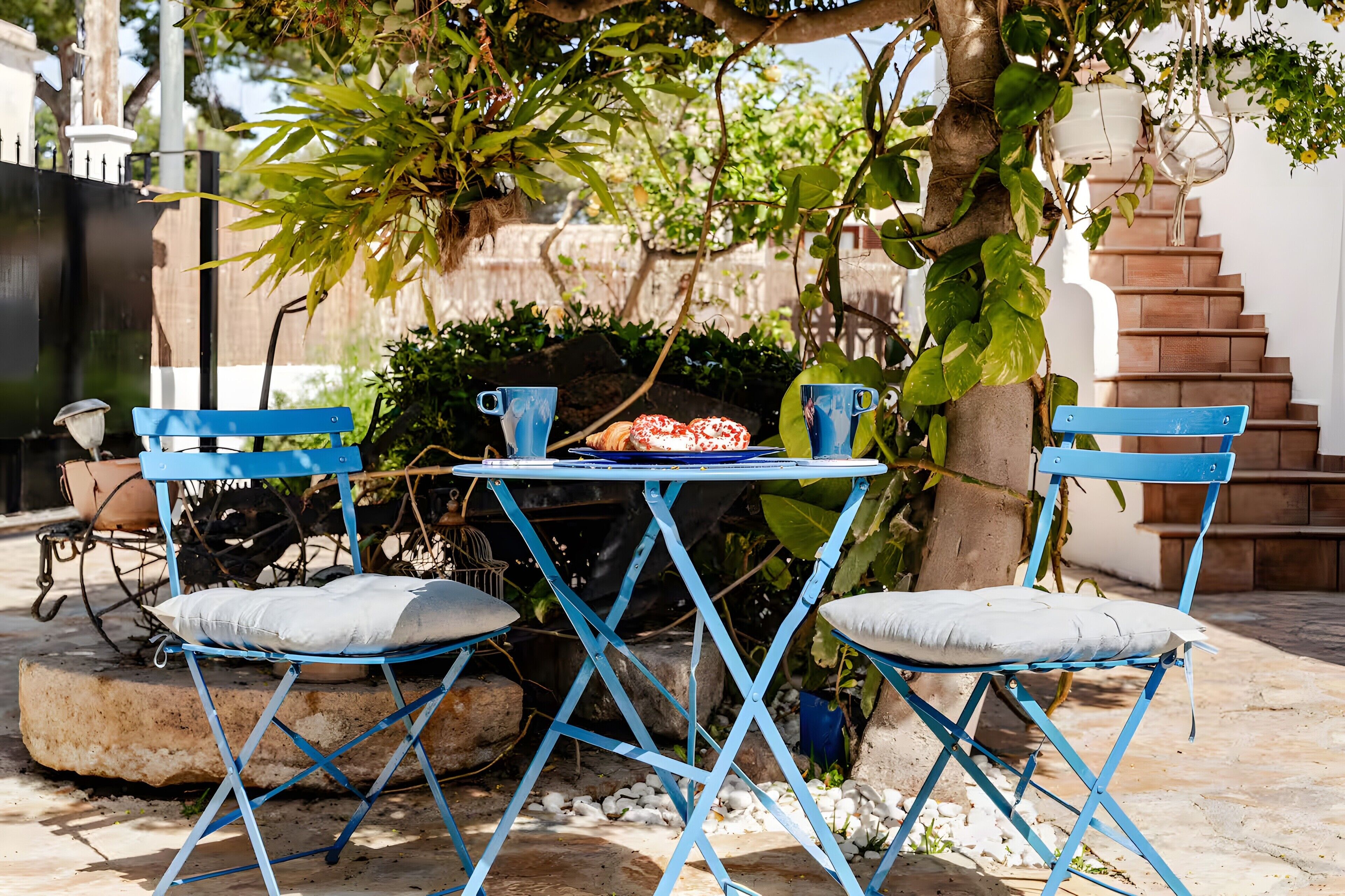 Une table en métal bleue, avec deux chaises, une assiette de nourriture et une plante en pot.