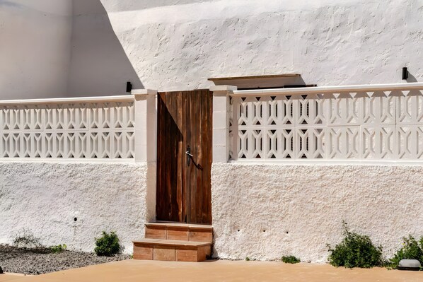 A white textured wall with a wooden door and steps leading to a balcony.