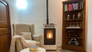A cozy room with a sofa, a table with books, a bookshelf with decorative items, and a wood-burning stove. - Vacation Home "Molino Son Moll" with Pool, Wi-Fi, Balcony, Garden & Terrace (Cala Ratjada)