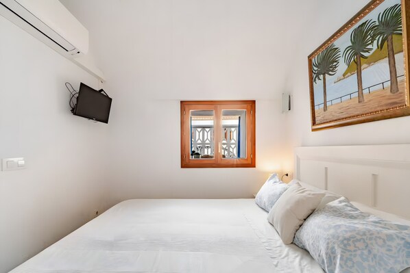 Quarto com cama, televisão na parede, janela com vista e um quadro.