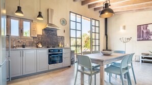 A modern kitchen with white cabinets, a stove, and a dining area with a table and chairs. - Holiday Home 'Cascada' with Mountain View, Private Pool and Wi-Fi (Costitx)