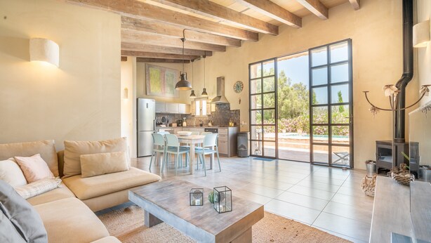 A spacious living area with a sofa, a coffee table, and a dining table with chairs. There is a kitchen in the background with a large window. - Holiday Home 'Cascada' with Mountain View, Private Pool and Wi-Fi (Costitx)