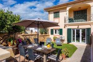 A patio with a table set for dining, outdoor chairs, a large umbrella, and a stone wall. - Apartamento "La Pergola" with Wi-Fi, A/C, Terrace & Garden (Font de Sa Cala)
