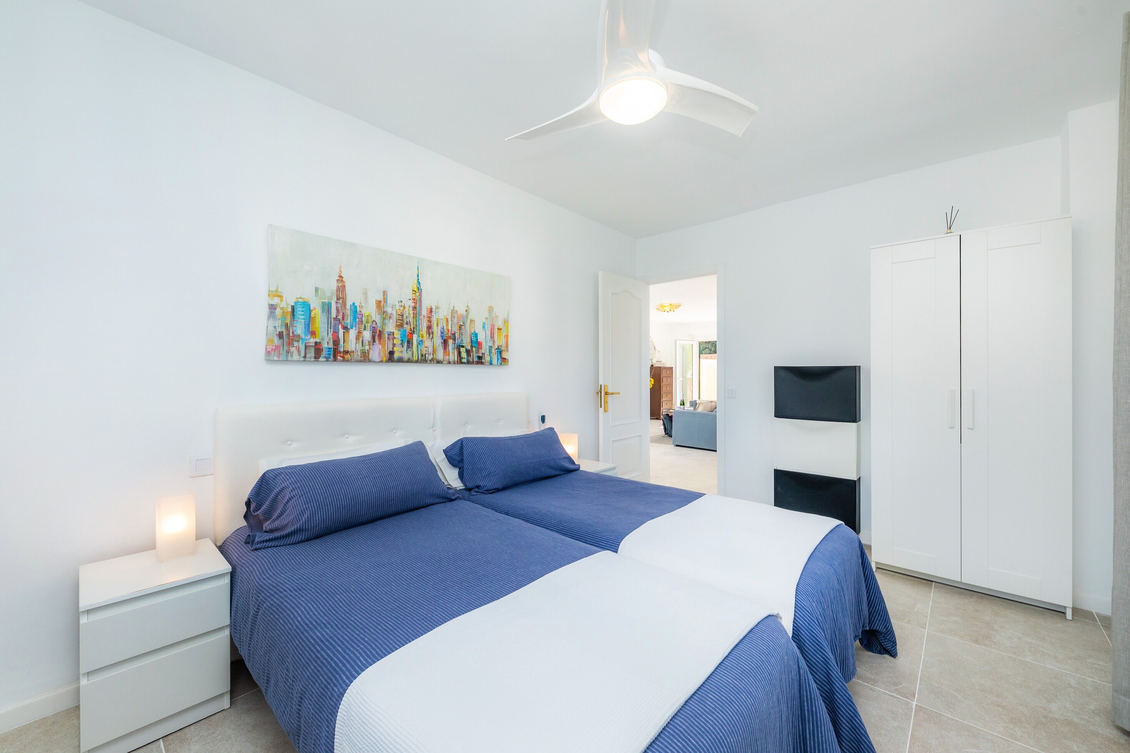 A modern bedroom with a bed, nightstands, a ceiling fan, a TV, and a wardrobe.