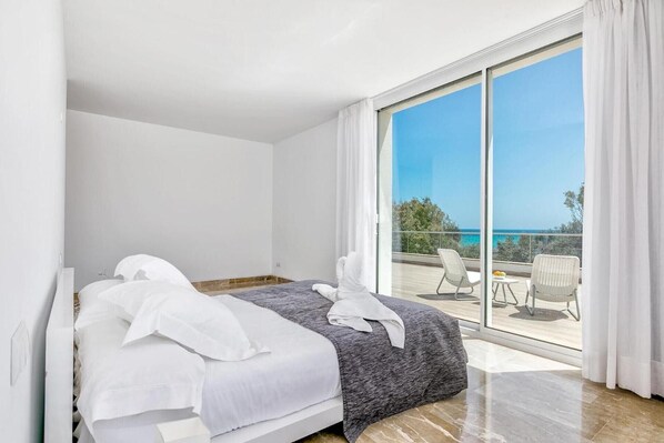 Une chambre d’hôtel avec un lit, une grande fenêtre et un balcon équipé de chaises.
