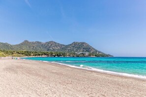 Une plage à l’eau turquoise et limpide, un rivage sablonneux et une montagne en arrière-plan.