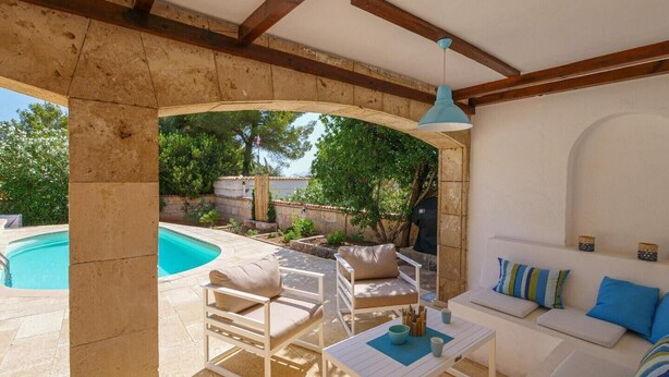 A covered outdoor seating area with a pool, white furniture, and a blue pendant light. - Villa Albatros near the Beach, with Sea View, Garden, Wi-Fi and A/C (Canyamel)