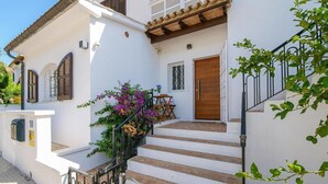 A white building with a wooden door, a staircase, and a small table with chairs outside. - Villa Albatros near the Beach, with Sea View, Garden, Wi-Fi and A/C (Canyamel)