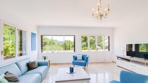 A spacious living room with a blue sofa, a coffee table, and a TV on a white cabinet. - Villa Albatros near the Beach, with Sea View, Garden, Wi-Fi and A/C (Canyamel)