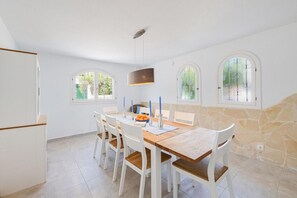 A dining area with a wooden table, white chairs, and a stone accent wall. - Villa Albatros near the Beach, with Sea View, Garden, Wi-Fi and A/C (Canyamel)