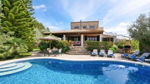 Un espace aménagé au bord de la piscine, avec une piscine carrelée, des chaises longues et un bâtiment doté d’un toit recouvert de tuiles.