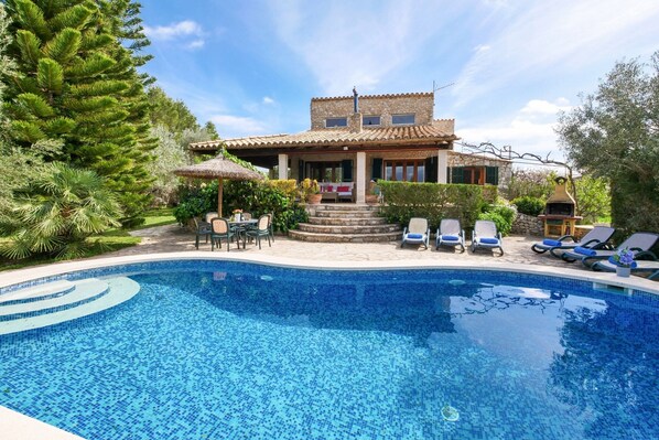 A poolside area with a tiled pool, lounge chairs, and a building with a tiled roof.