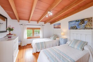 A bedroom with two beds, wooden beams on the ceiling, a painting on the wall, and a window with curtains.
