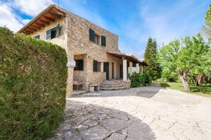 A stone house with a stone pathway leading to the entrance, a covered porch, and a well-maintained garden.
