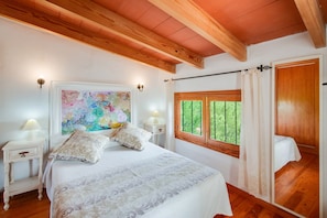 A bedroom with a bed, a nightstand, a lamp, a painting, a window with curtains, and a wooden ceiling. - Finca Can Reure with Mountain View, Wi-Fi Pool, Garden & Terrace (Inca)