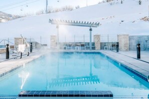 Ein Swimmingpool mit einer Pergola, Liegestühlen und Blick auf eine verschneite Landschaft.