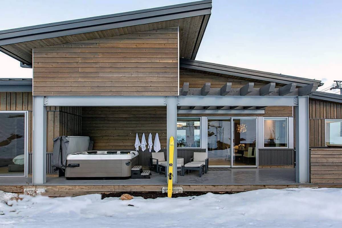 Ein modernes Haus mit überdachter Terrasse, Whirlpool und einer Schiebetür zu einem Innenbereich.