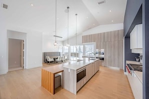 A modern kitchen with a central island, pendant lighting, and a view to the dining area.